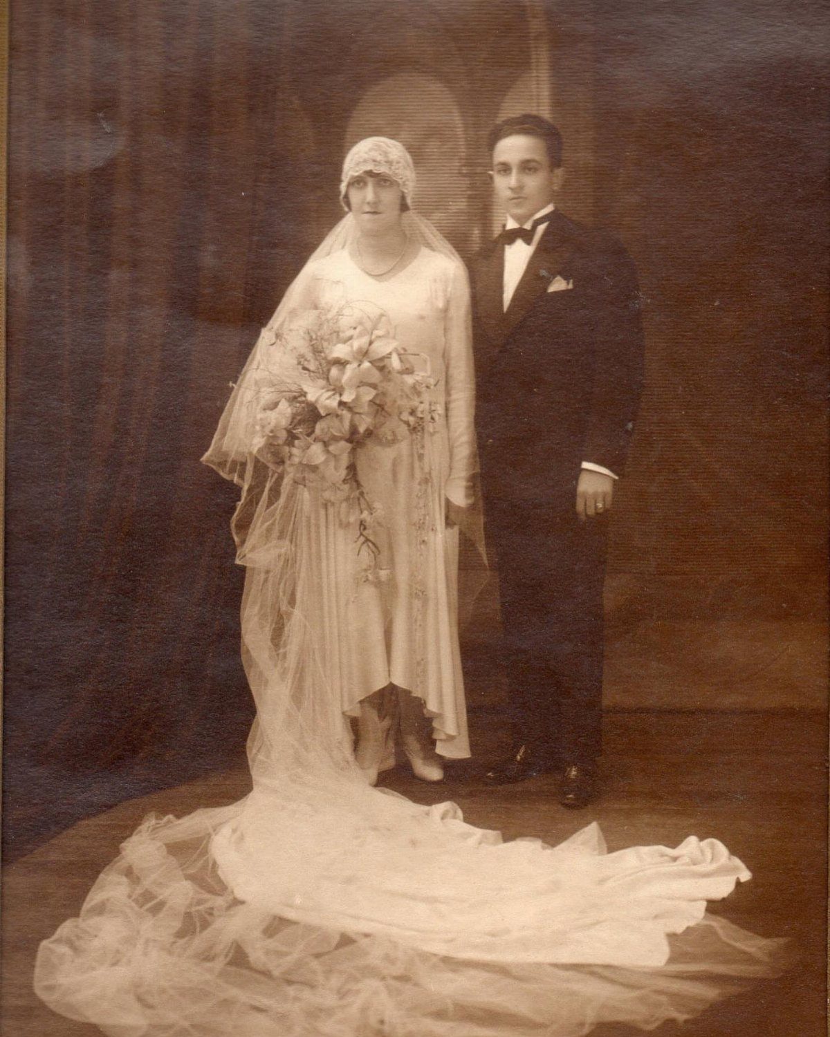 Bride in a 1920s wedding dress and groom in a tuxedo posing together.