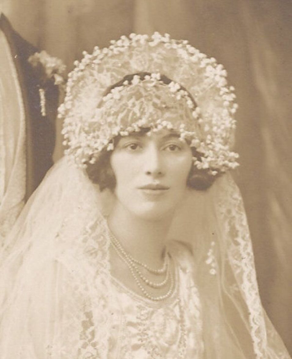 Woman wearing an ornate floral Juliet cap, lace veil, and pearl necklace.