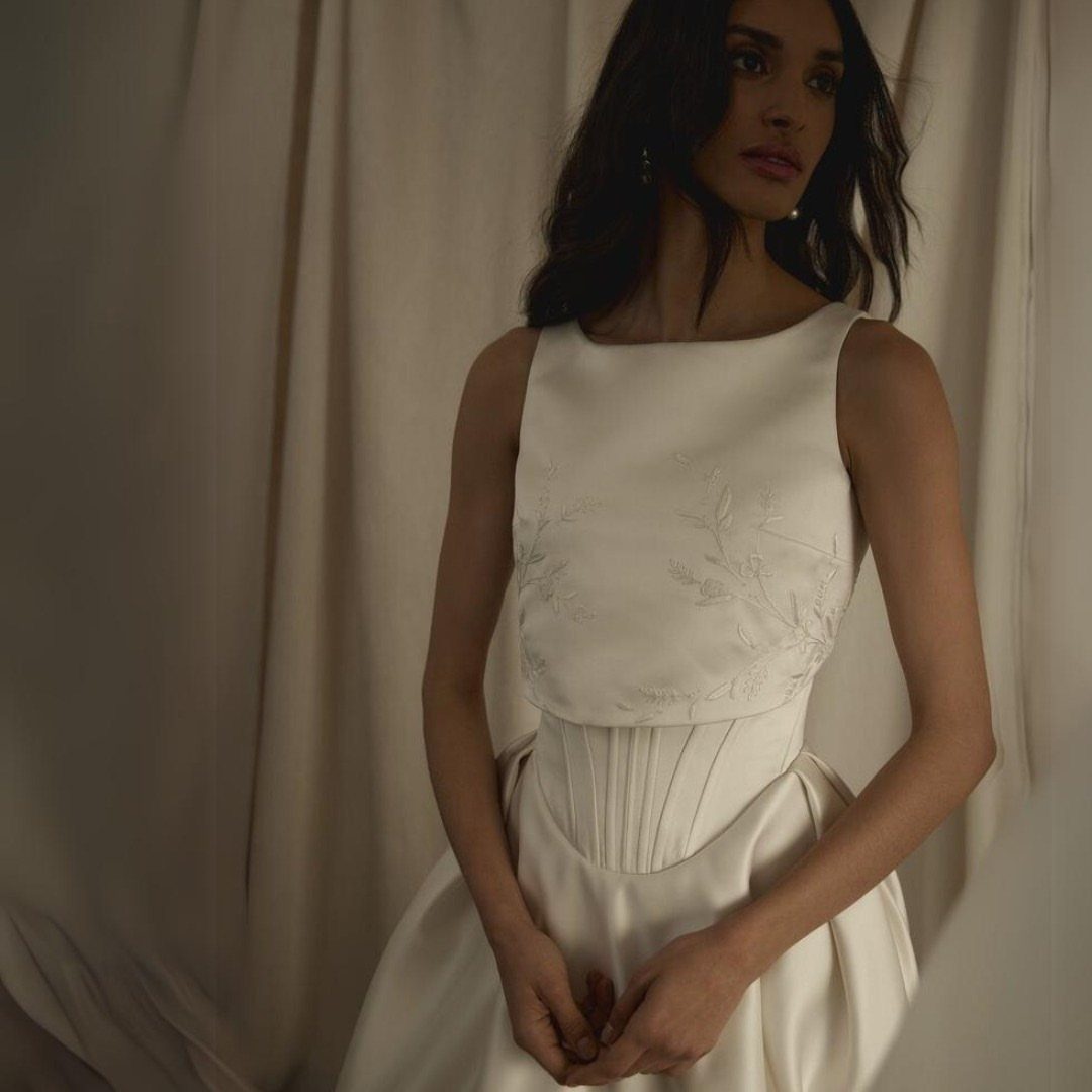 Woman in a white wedding gown featuring a structured basque waistline and embroidery.