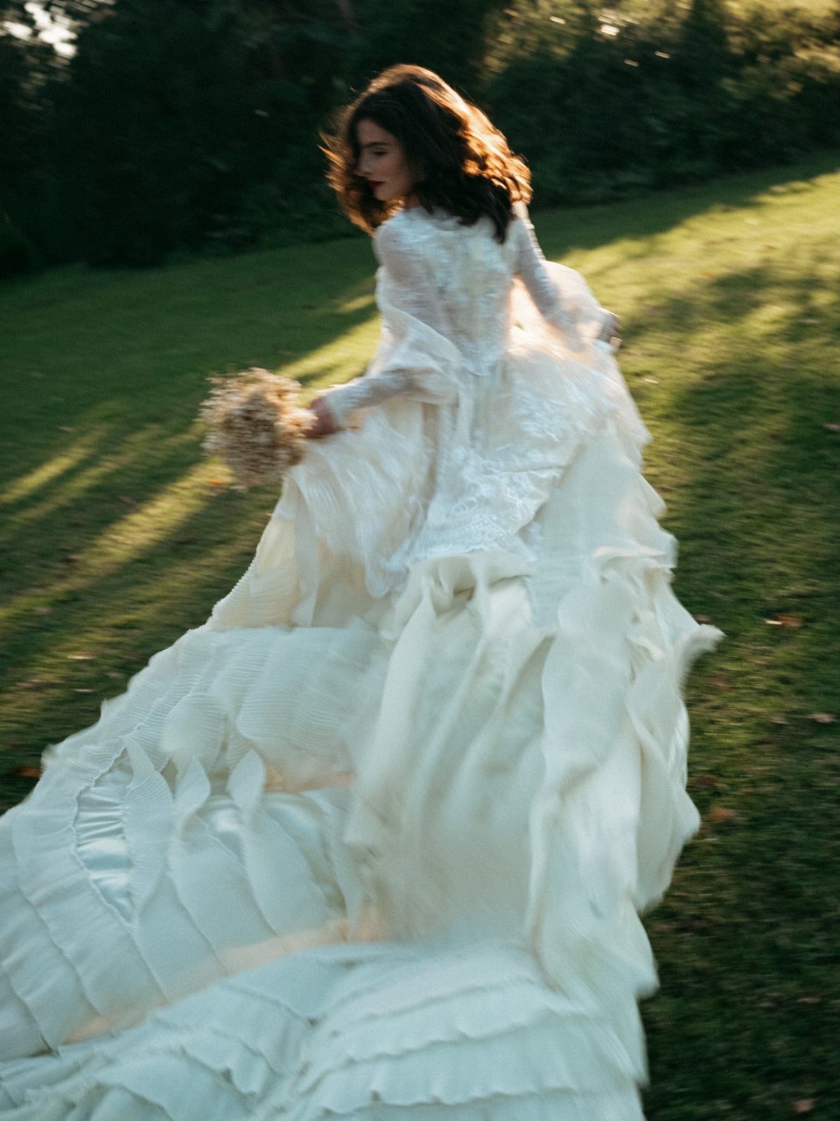 Woman in white lace wedding dress with a large ruffled train in a field