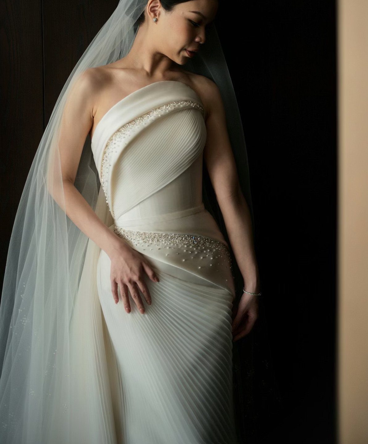 Woman in a cream strapless wedding gown with pleated draped fabric and beaded accents.