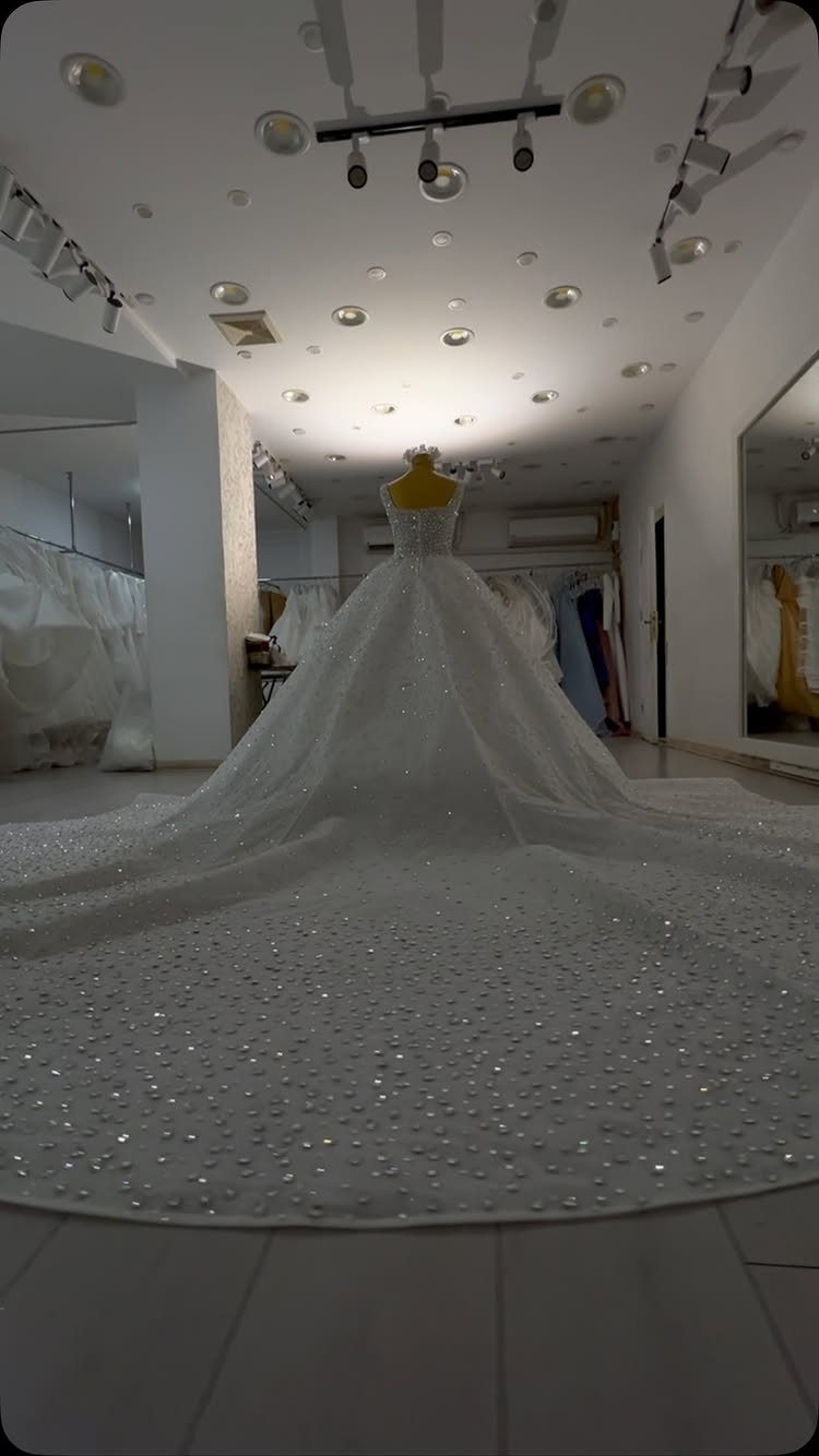 White beaded wedding dress with a long train on a yellow mannequin