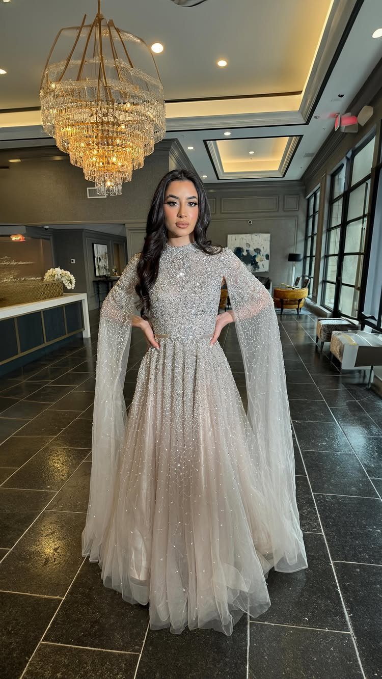 Woman in a shimmering champagne beaded gown with long flowing beaded sleeves.