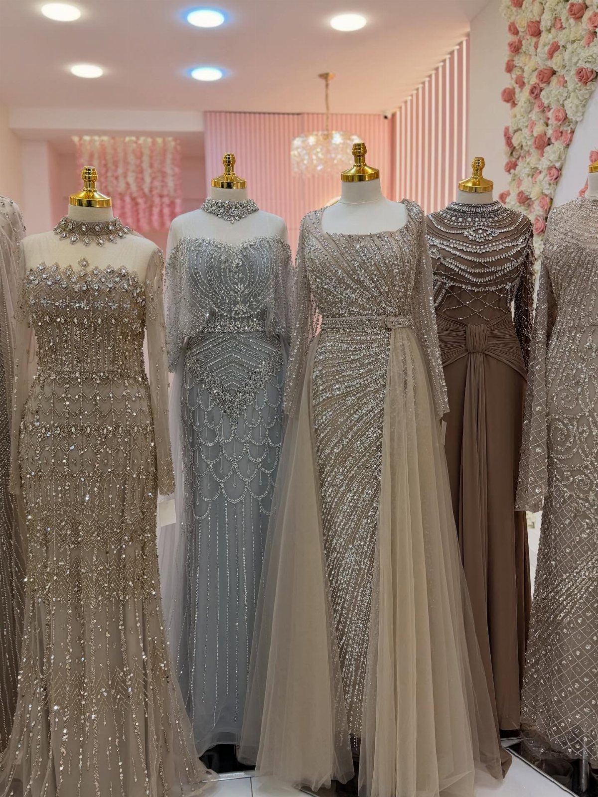 Beaded wedding gowns in silver and champagne displayed on mannequins in a boutique.