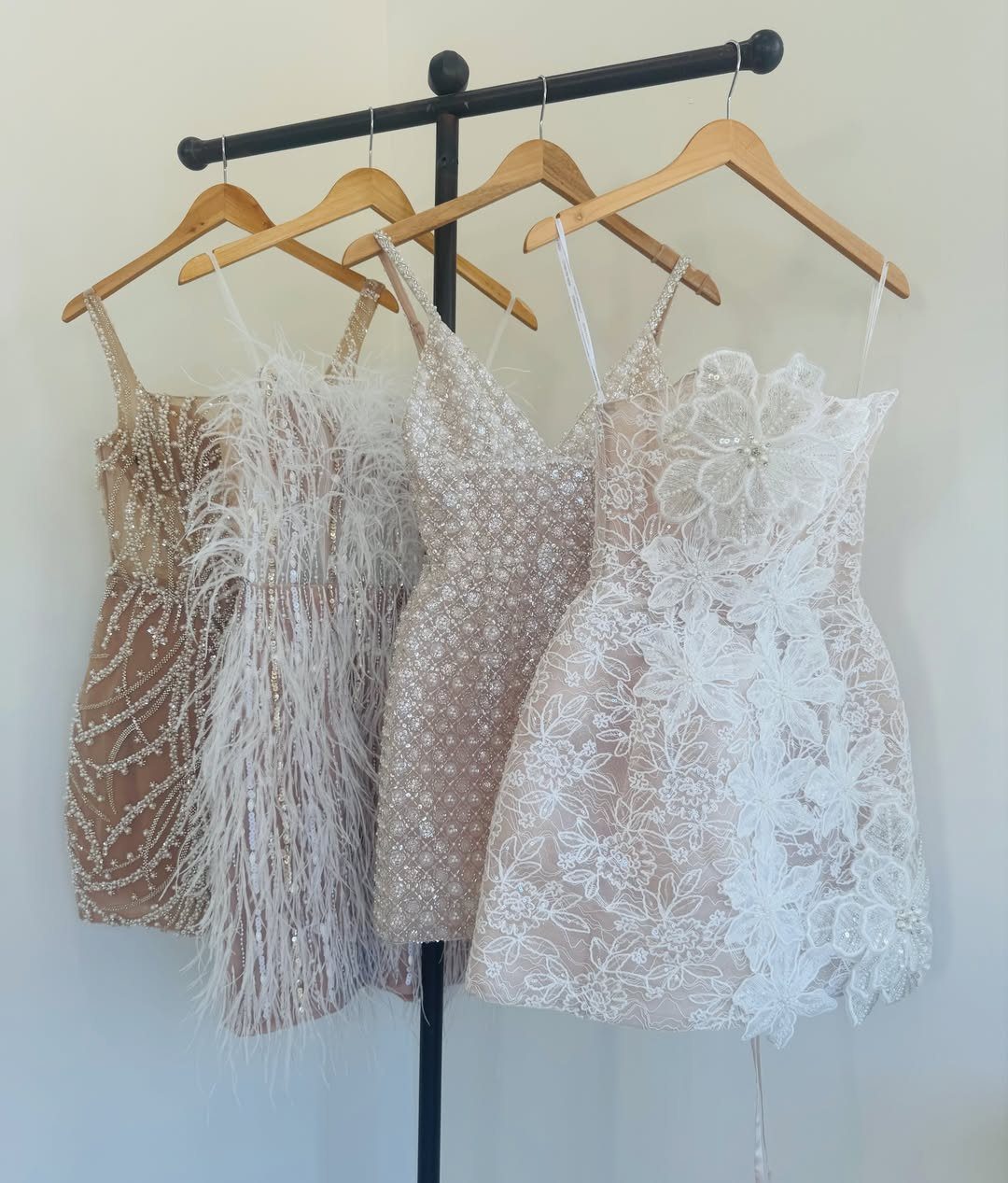 Four ornate beaded and lace short wedding dresses hanging on a black rack