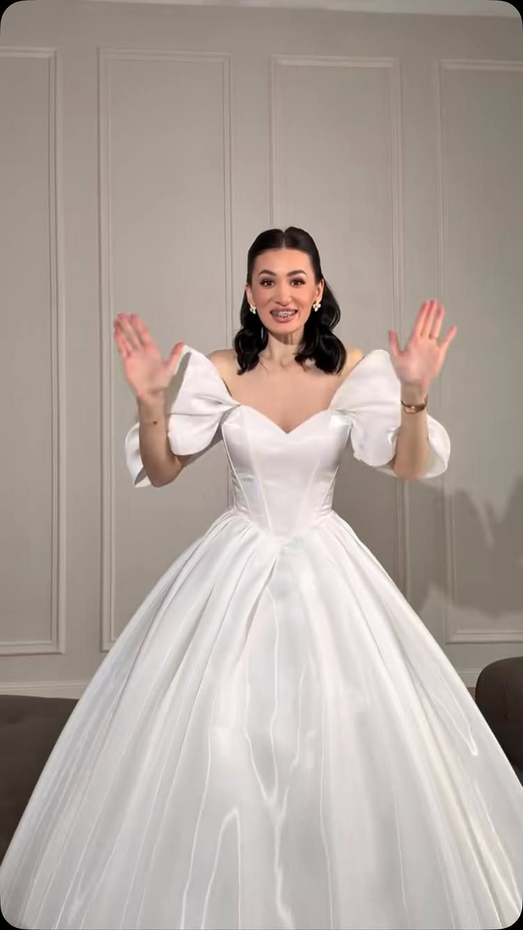 Woman in a voluminous white satin ballgown wedding dress posing against grey walls