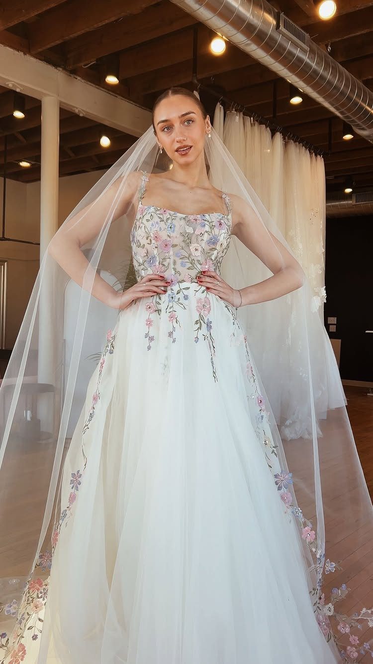Woman in a white wedding gown with vibrant colorful floral embroidery and a veil.