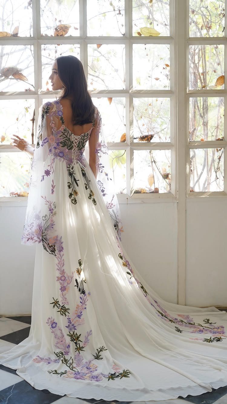 Woman wearing a white wedding dress with purple floral embroidery and a sheer cape