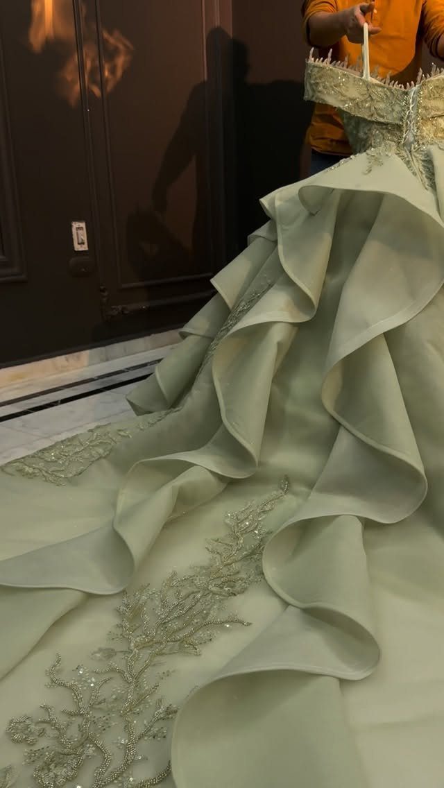 Sage green wedding dress with voluminous ruffles and silver embroidery on the fabric.