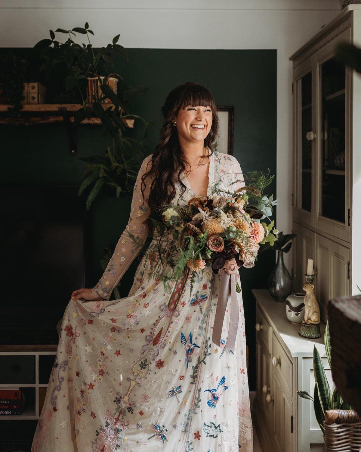 Woman in a white gown with colorful floral embroidery holding an autumn bouquet