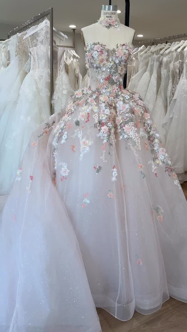 White wedding dress on a mannequin decorated with colorful 3D floral appliqués.