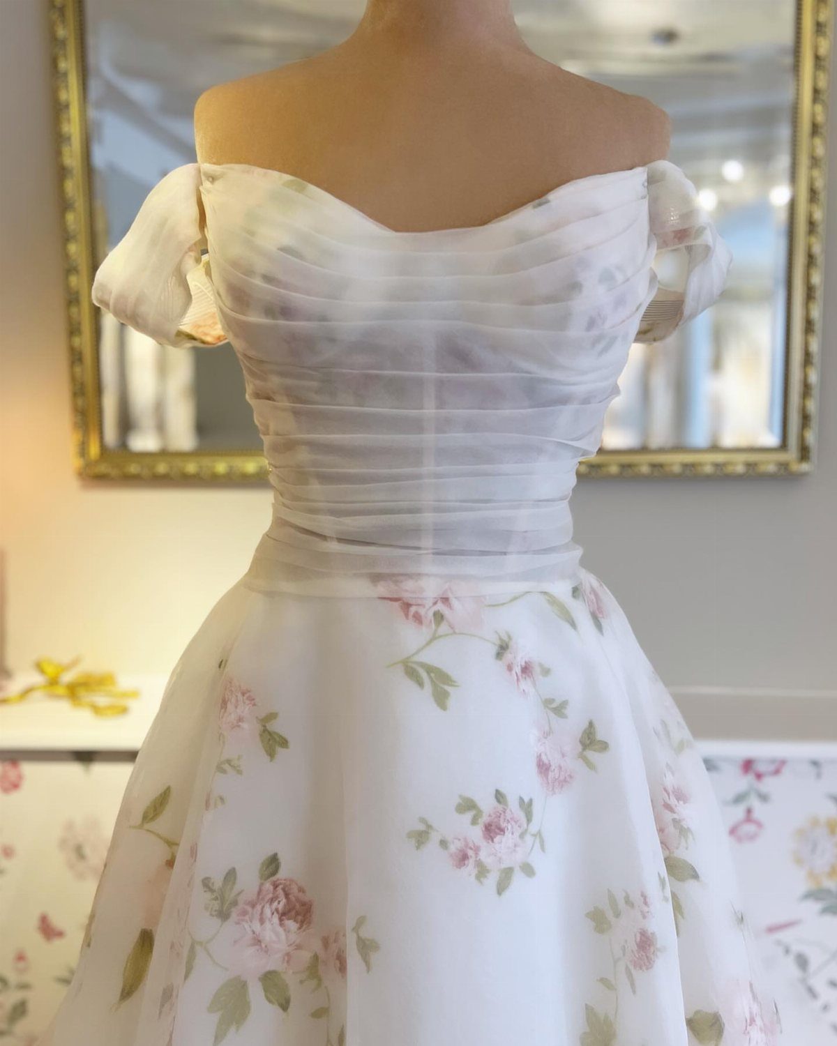 Off-the-shoulder white wedding dress with ruched bodice and pink floral print skirt.