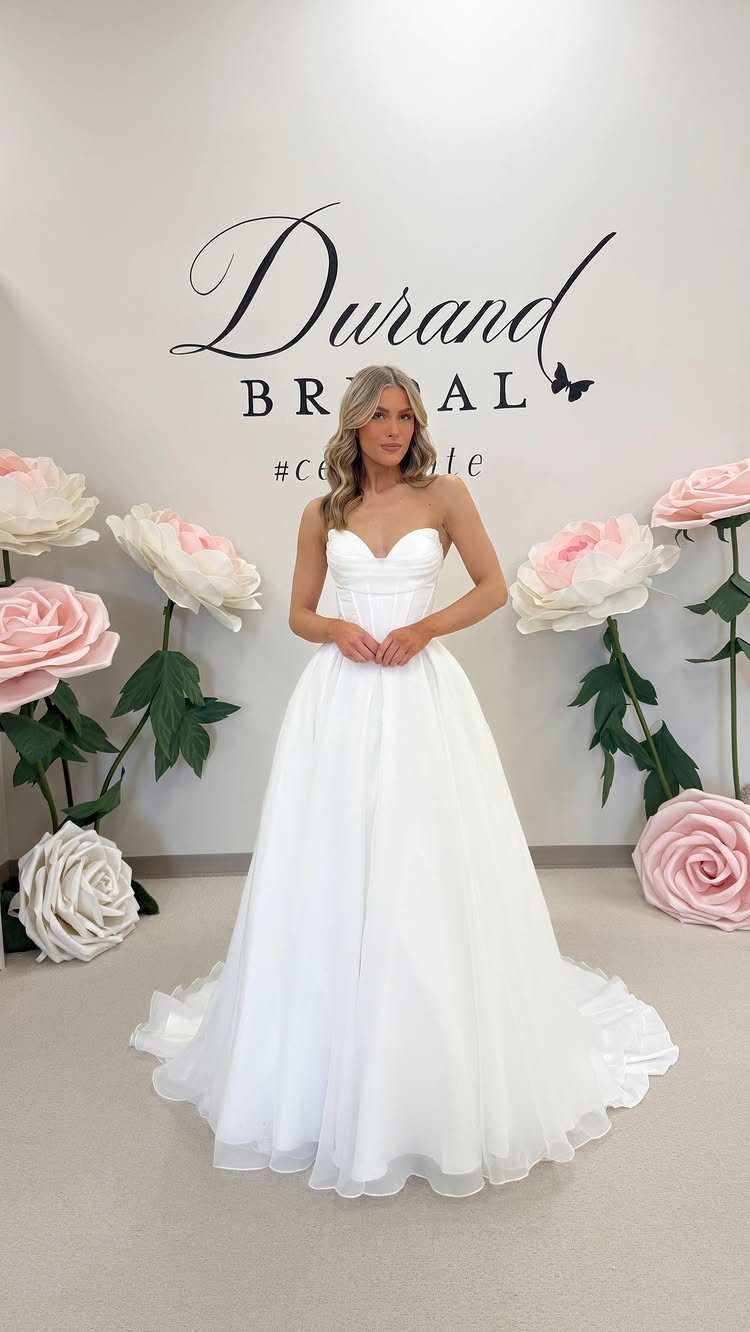 Woman in a strapless white wedding gown standing among large paper flowers.