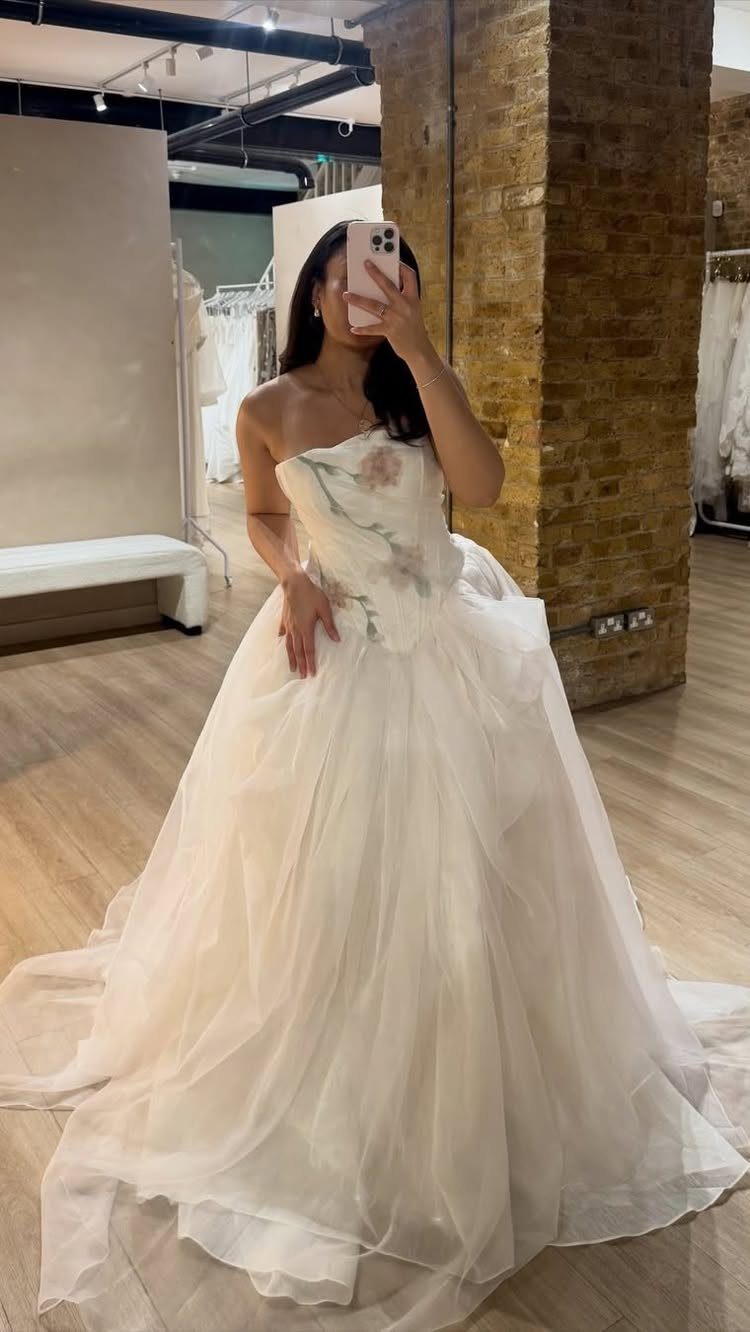 Woman in a voluminous white layered organza wedding dress taking a mirror selfie.