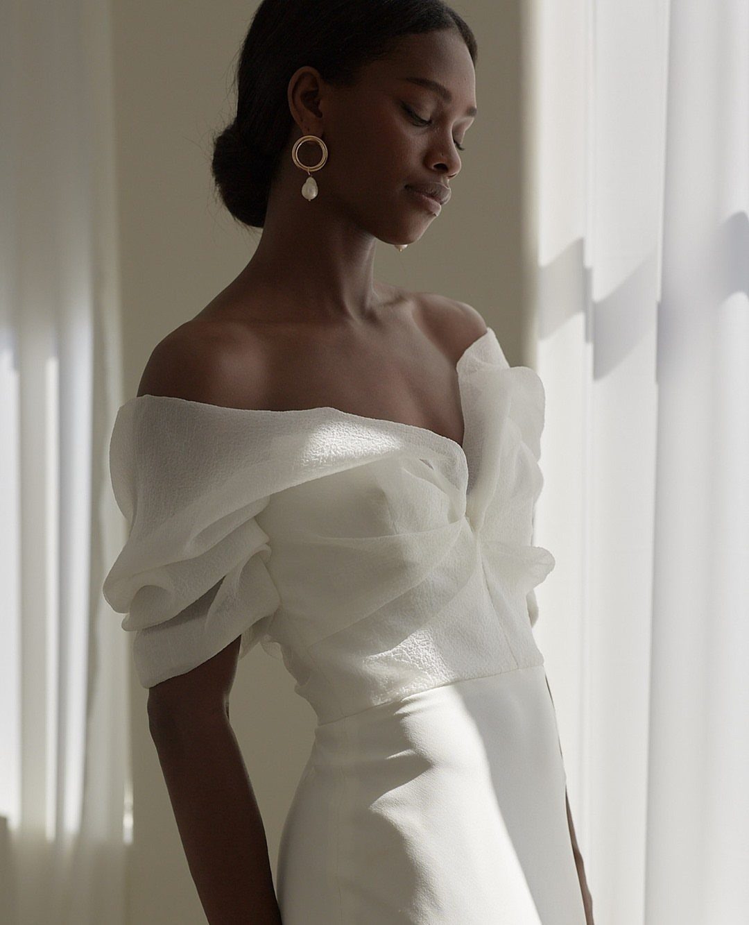 Woman wearing a minimalistic white wedding dress with a draped organza bodice.
