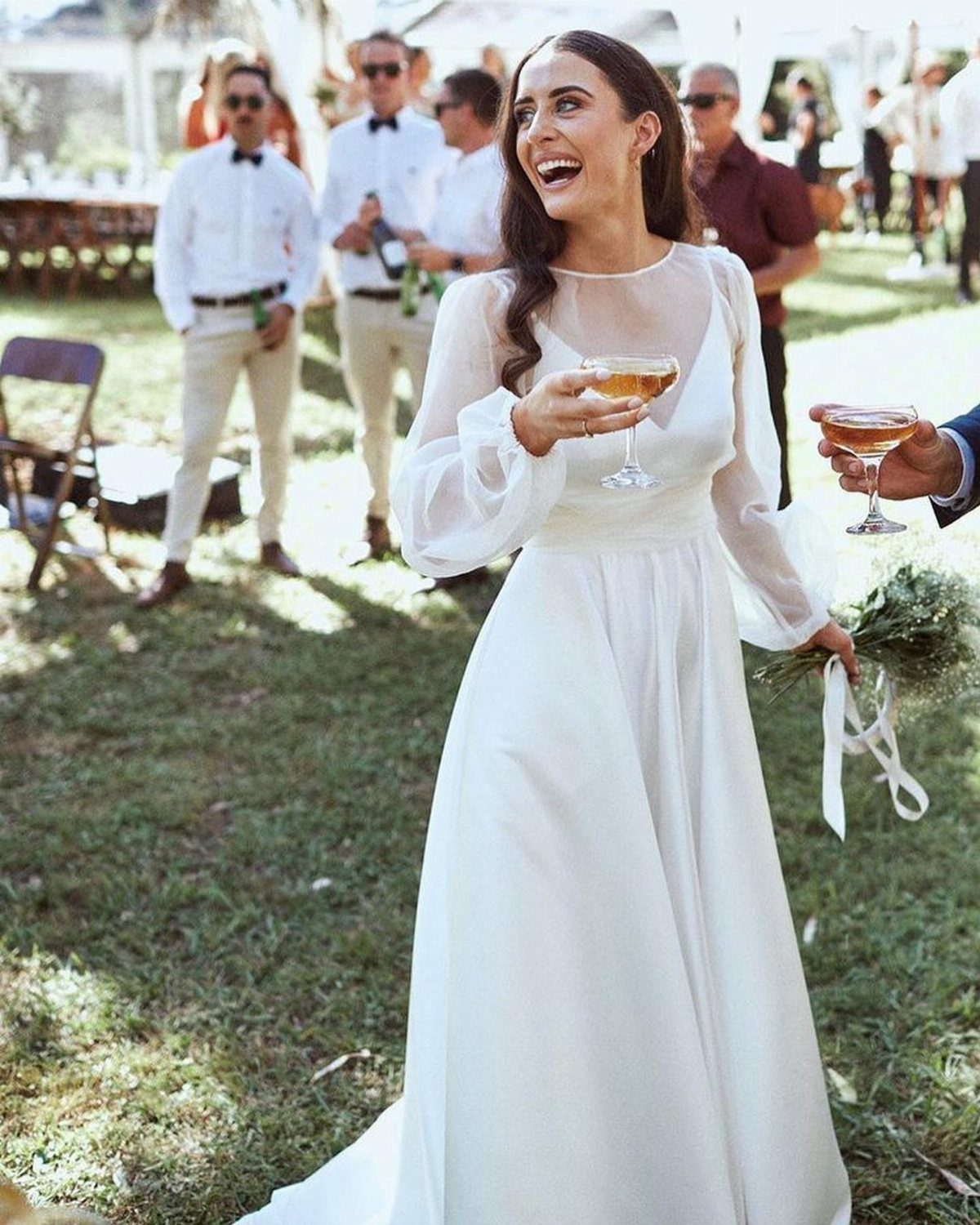 Woman in white organza wedding dress laughing and holding a drink outdoors.