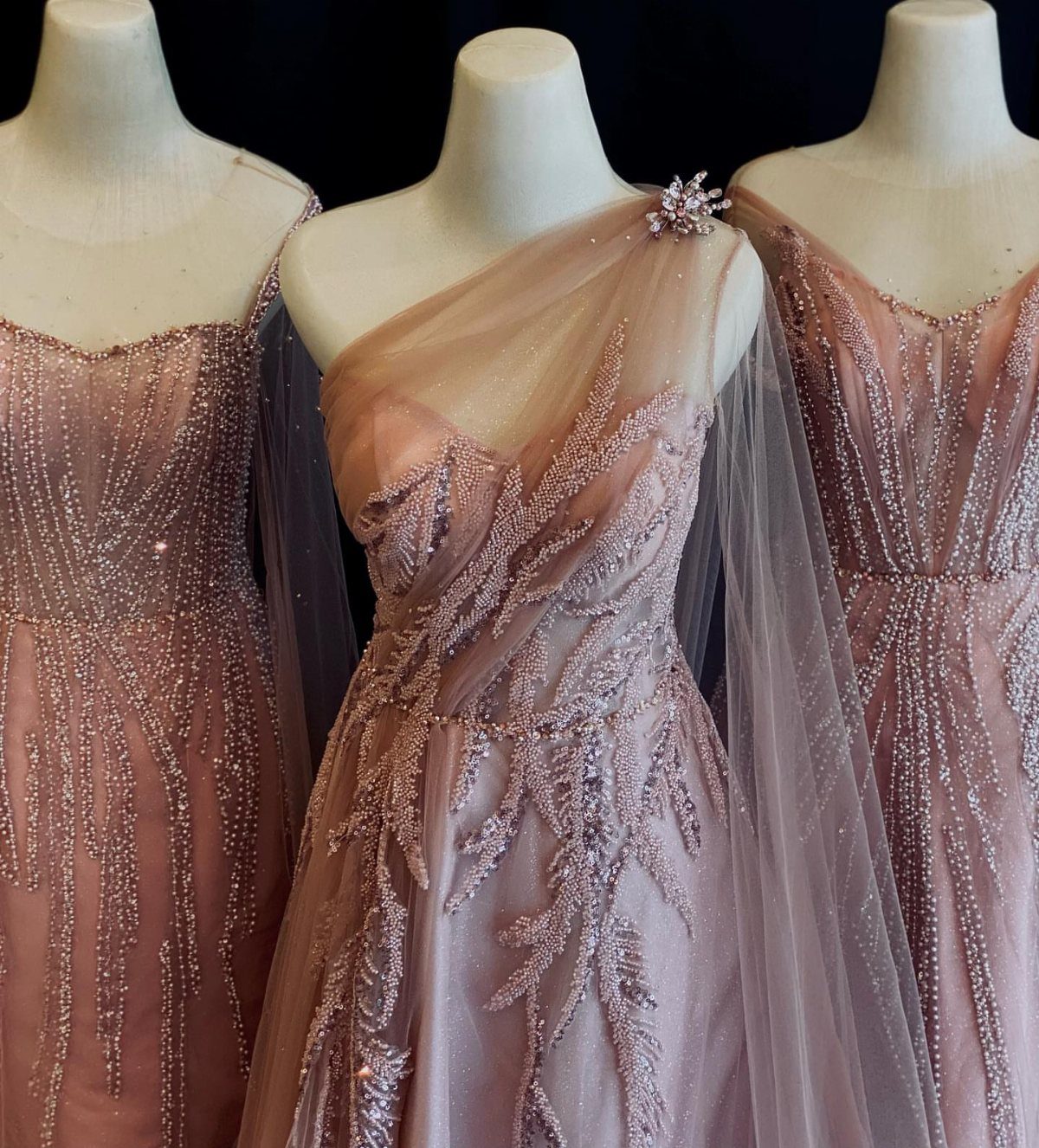 Three dusty pink gowns with sparkling beadwork displayed on white mannequins.