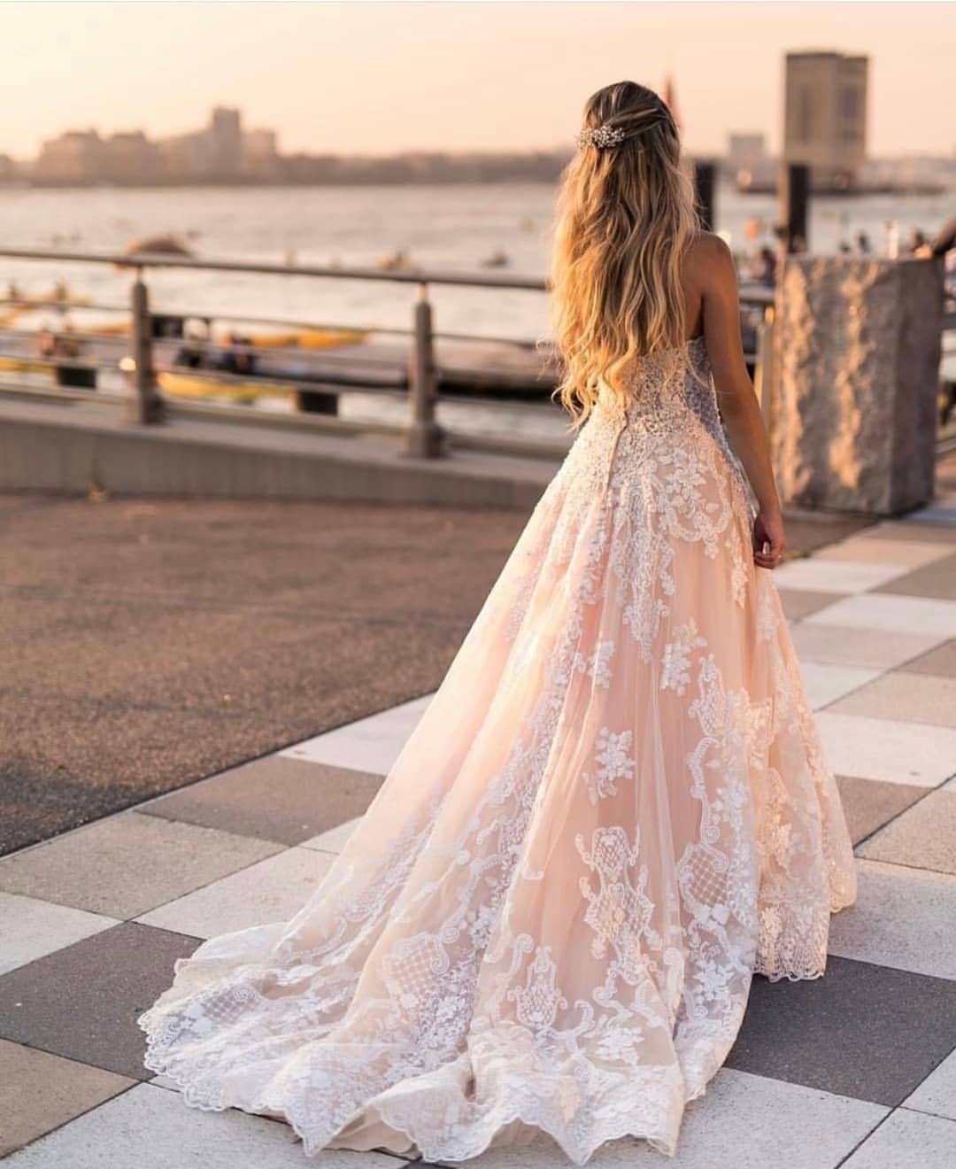 Woman in a pale pink wedding gown with white lace embroidery by the water