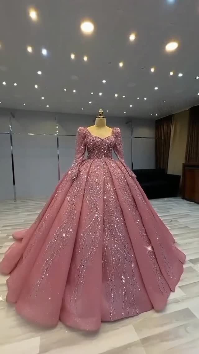 Sparkling pink ballgown wedding dress with long sleeves on a mannequin.