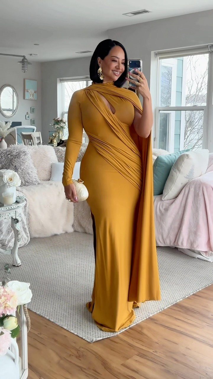 Woman in a long-sleeved mustard yellow gown posing for a mirror selfie indoors.