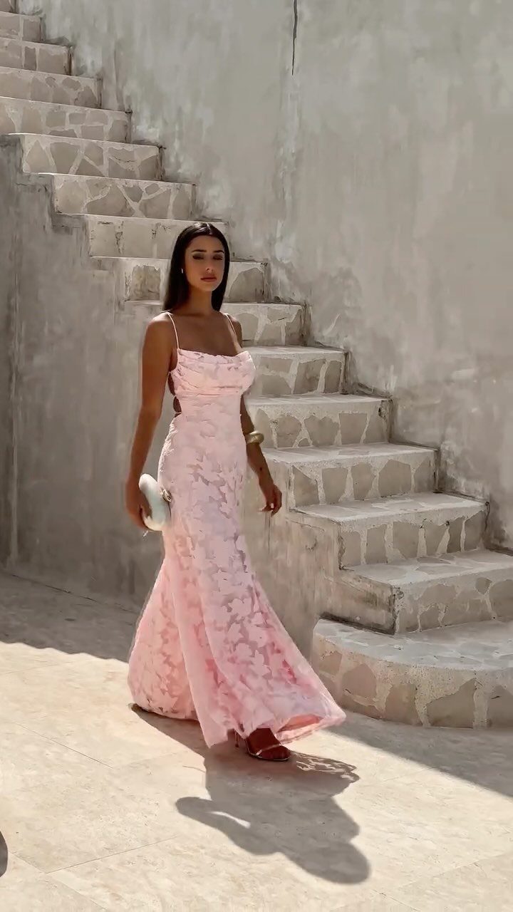 Woman in a light pink lace maxi dress standing by concrete stairs.
