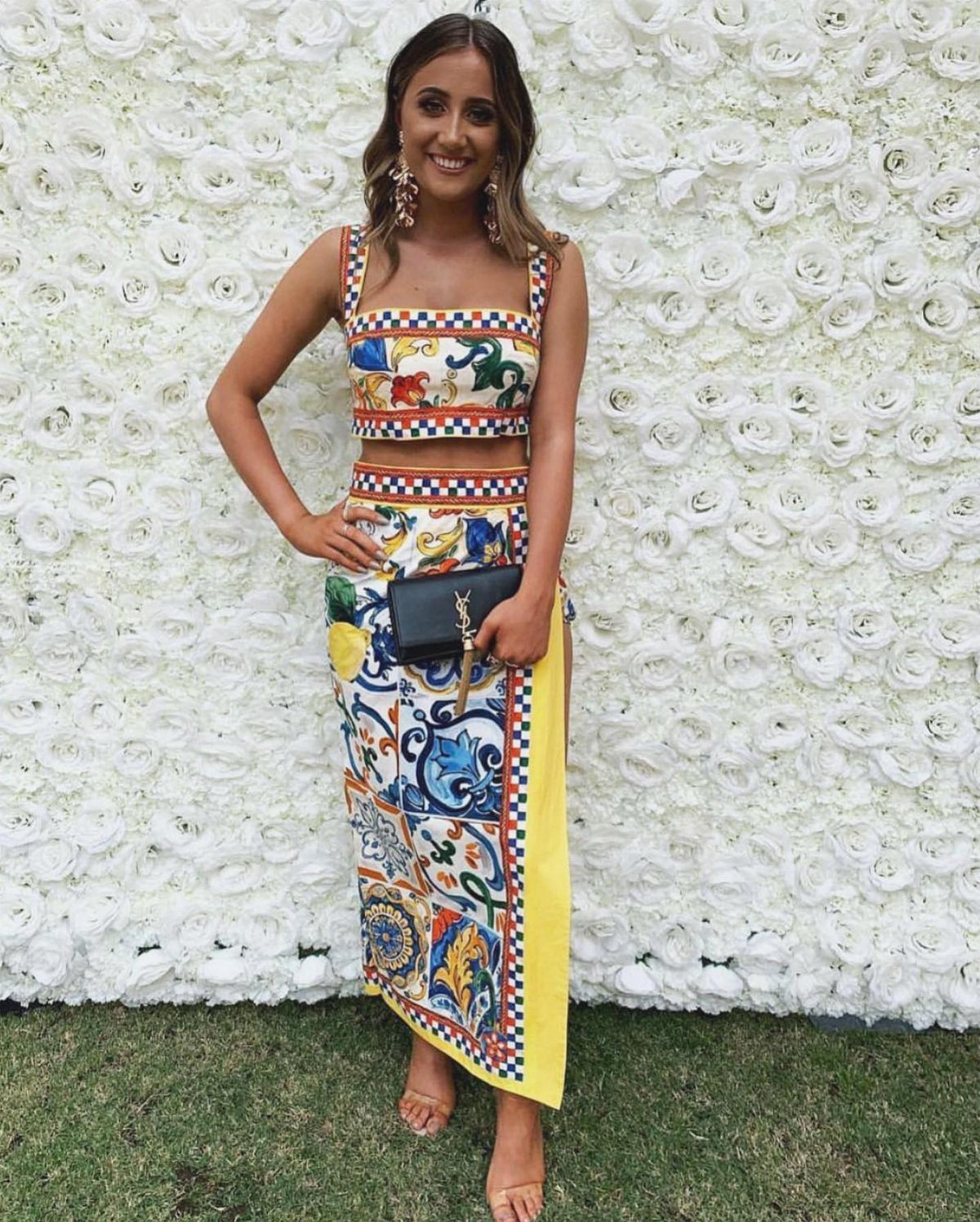 Woman wearing a colorful patterned two-piece set posing against a white flower wall