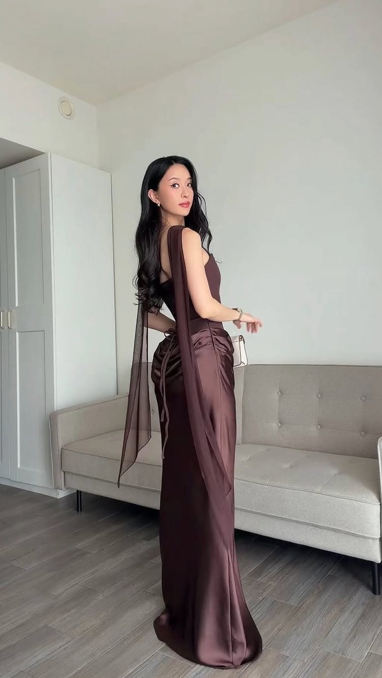 Woman wearing a long brown satin evening gown and sheer shawl indoors.
