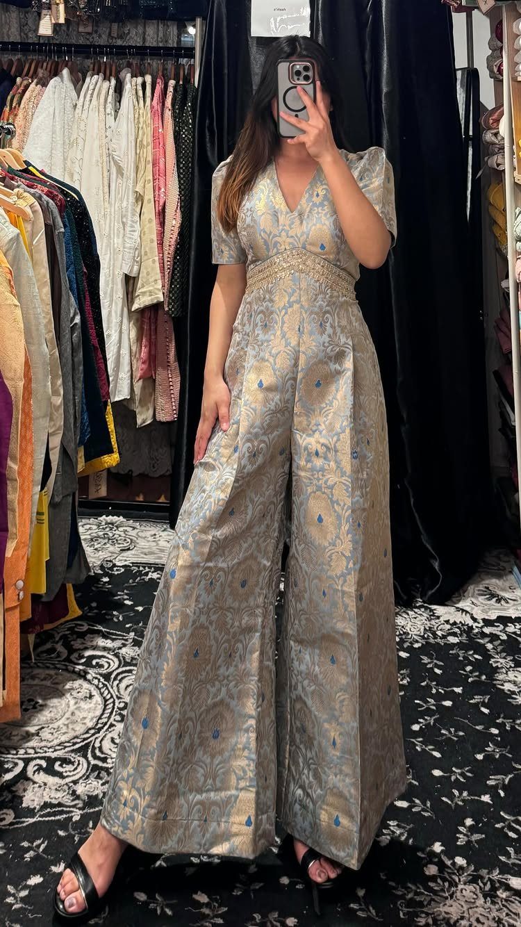 Woman wearing a light blue and gold patterned wide-leg jumpsuit in a boutique.