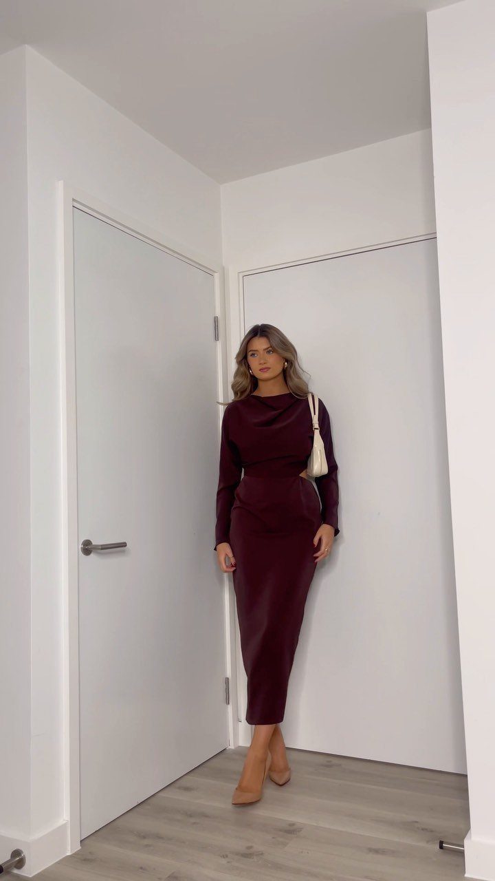 Woman in a burgundy long-sleeved midi dress and nude heels in a hallway