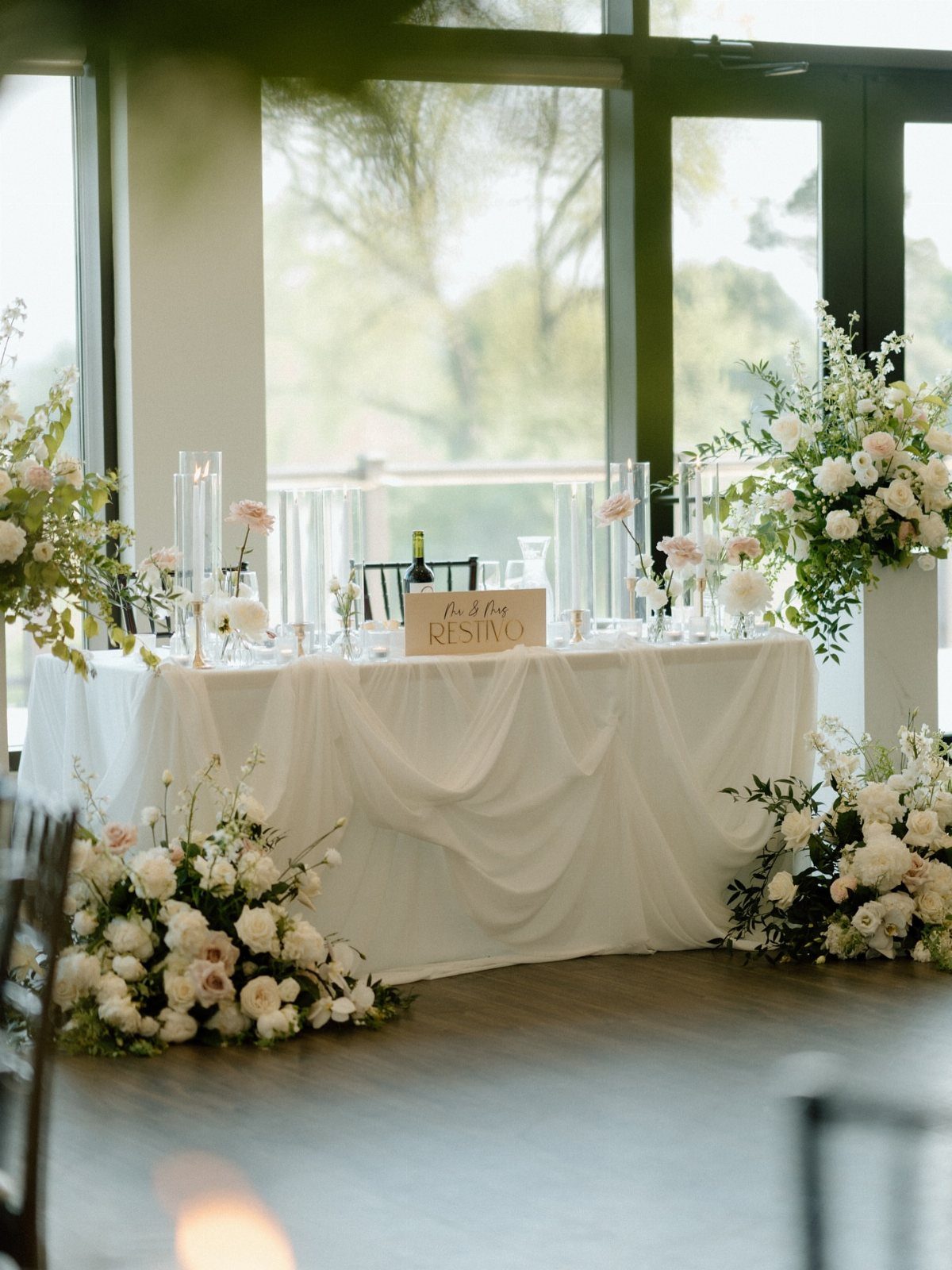Long white draped head table decorated with white and blush floral arrangements.