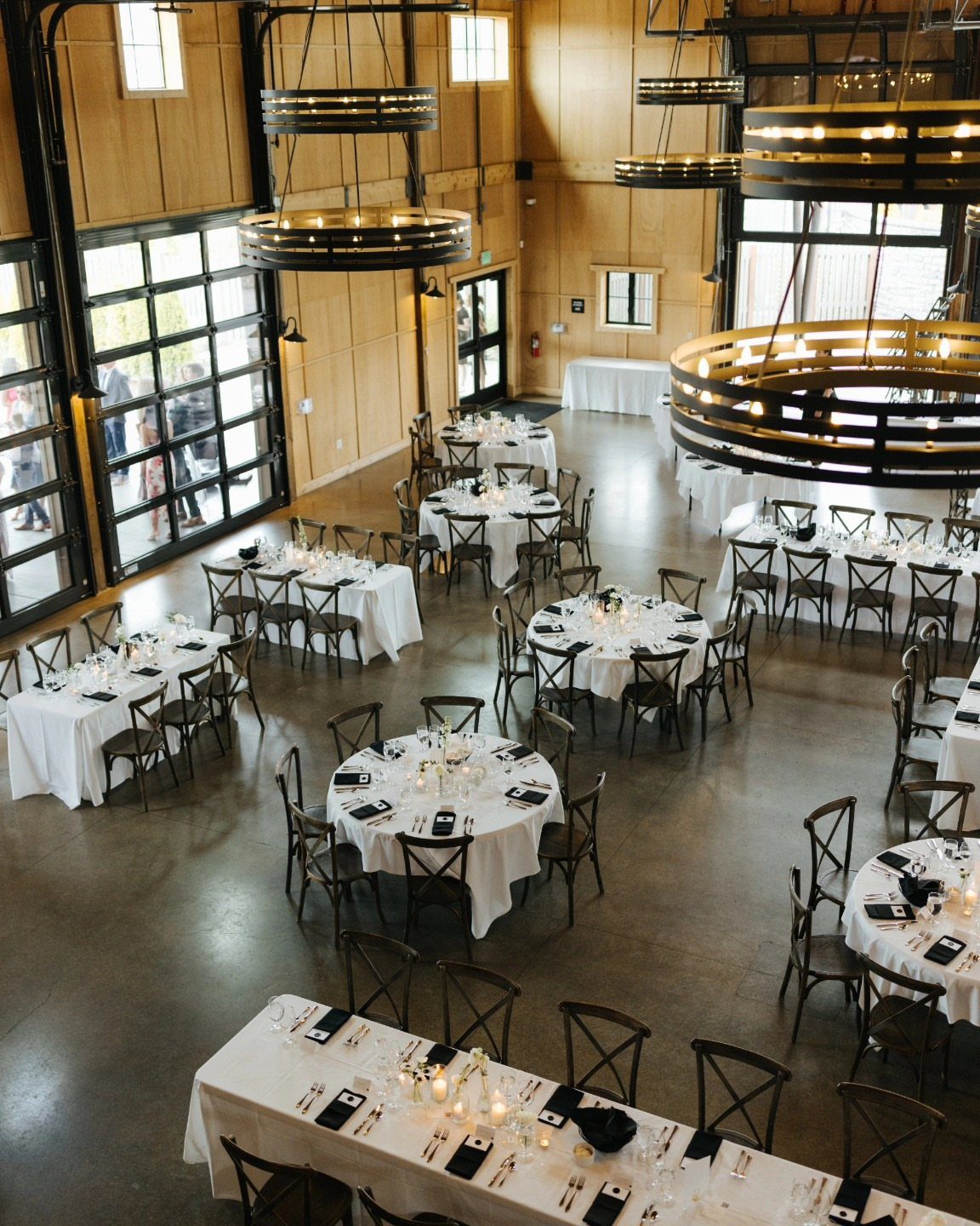Wedding guest tables with white linens and dark wooden chairs in a rustic hall.