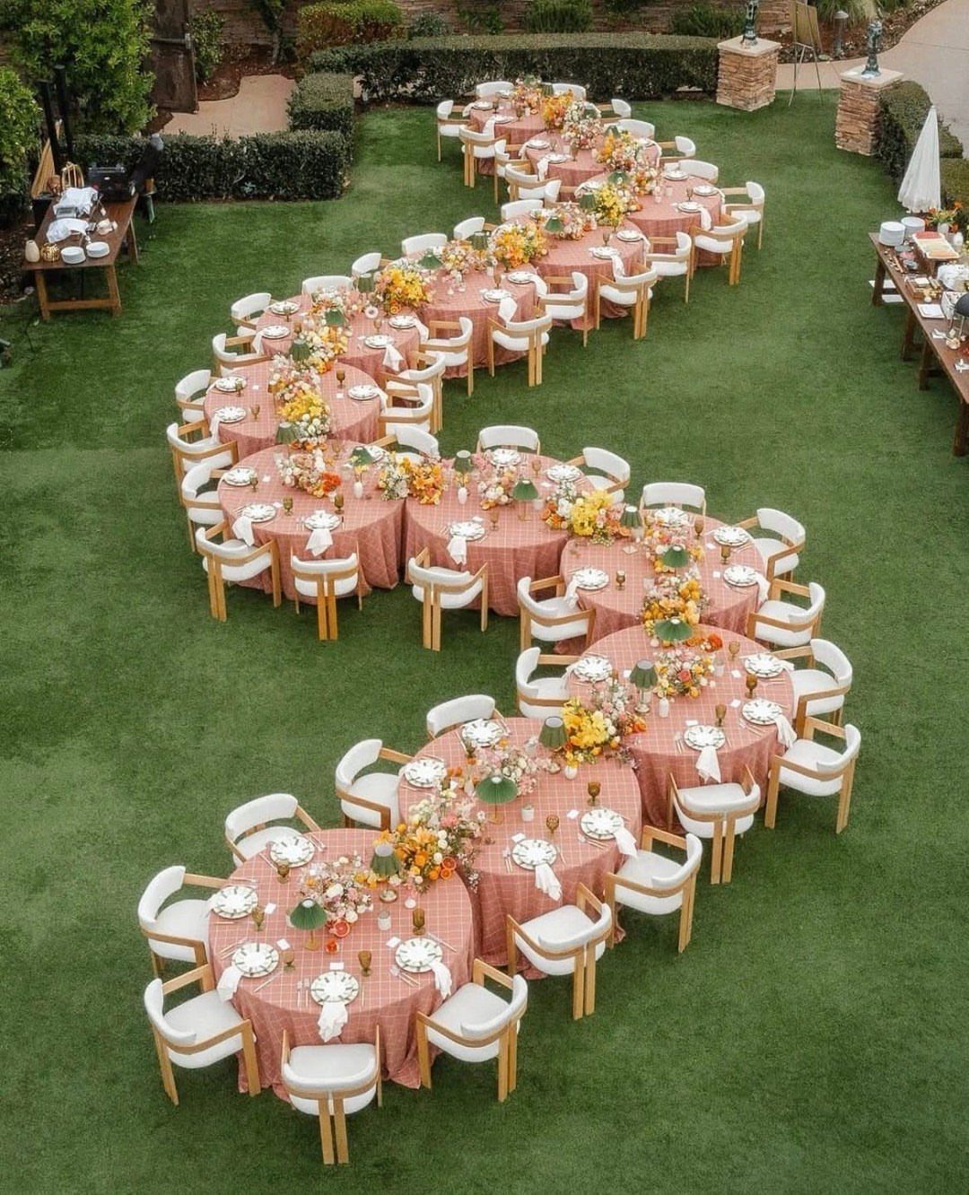 Round tables with pink linens and white chairs arranged on a green lawn.