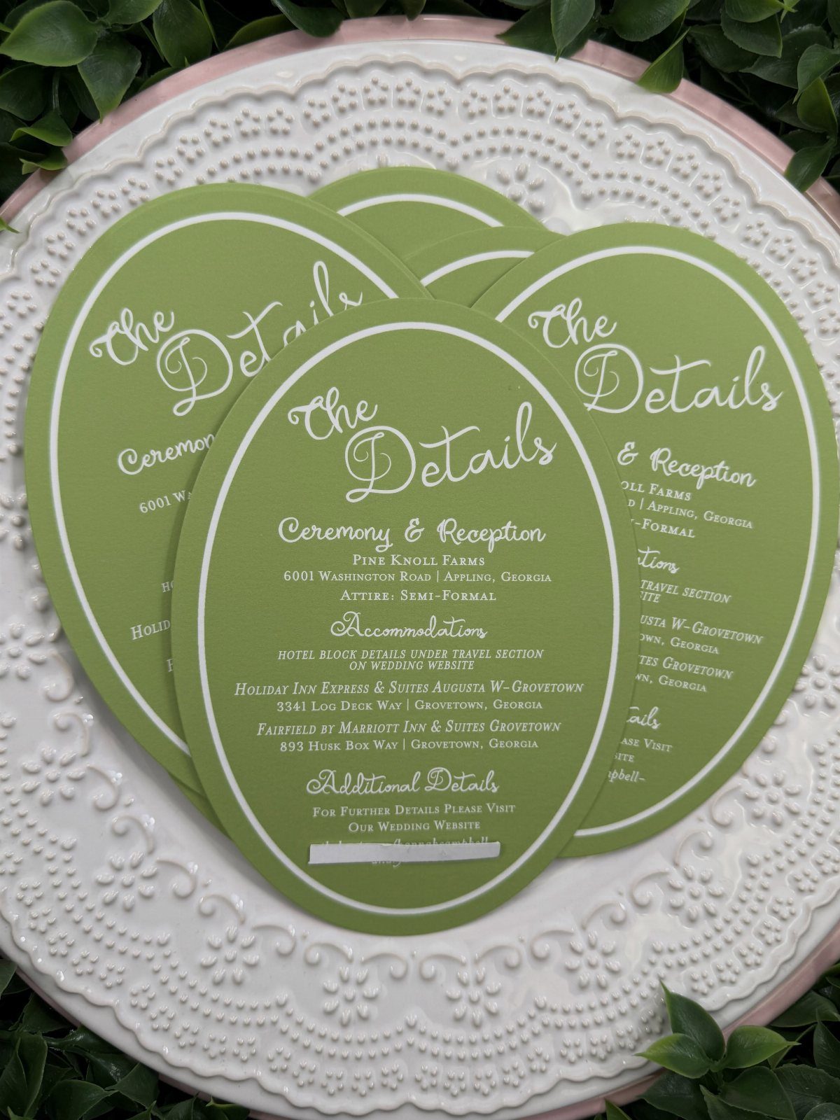 Green oval wedding detail cards with white text on a white lace plate.