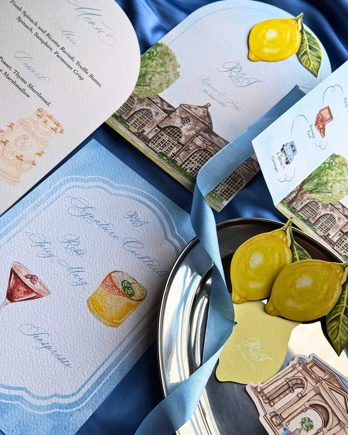 Wedding day stationery suite with lemon illustrations and a blue ribbon on fabric.