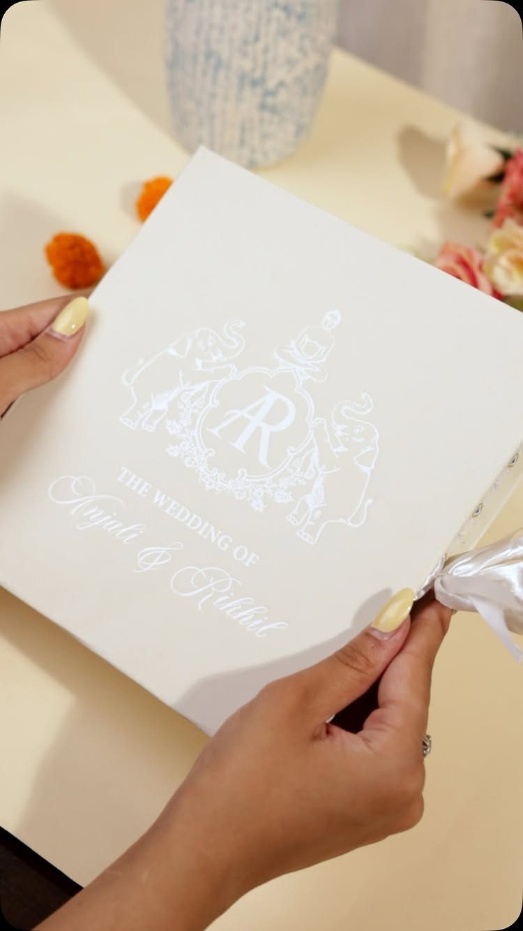 White embossed wedding invitation with a decorative crest held by two hands.
