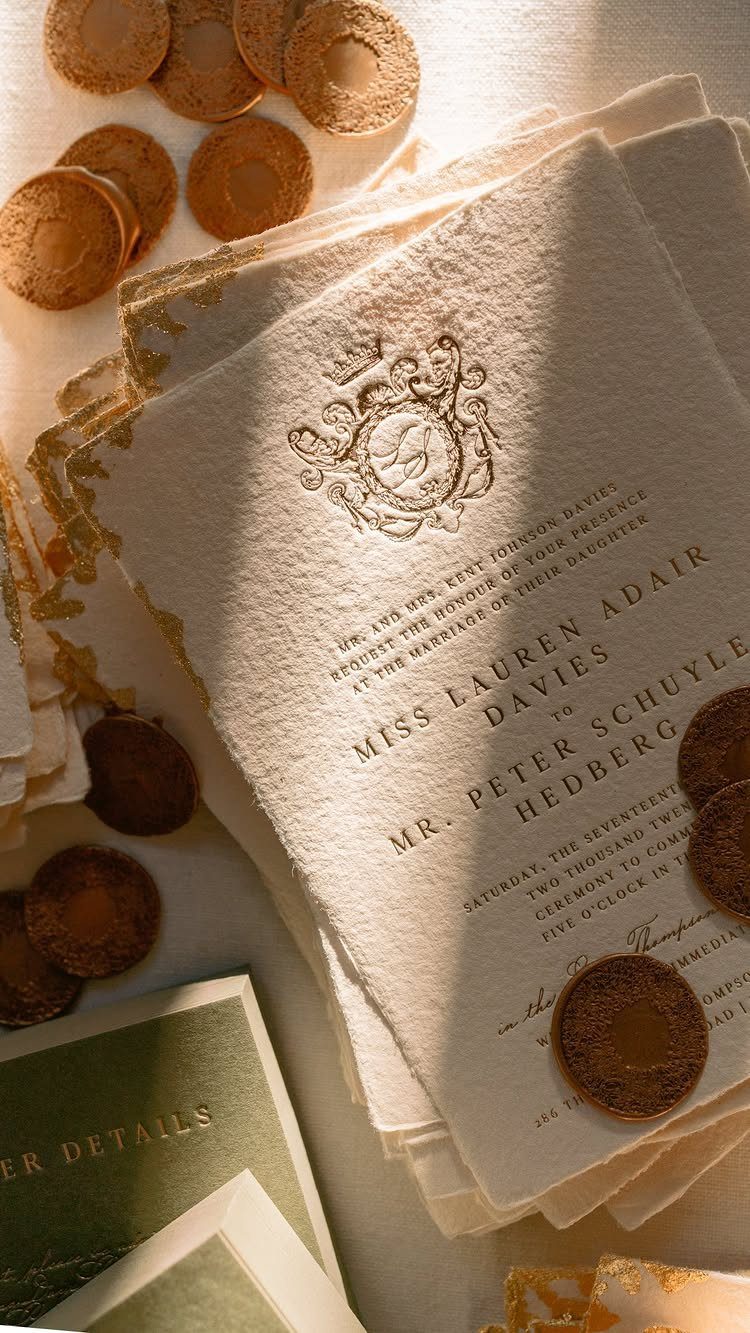 Cream textured wedding invitation with debossed lettering and gold wax seals on white surface