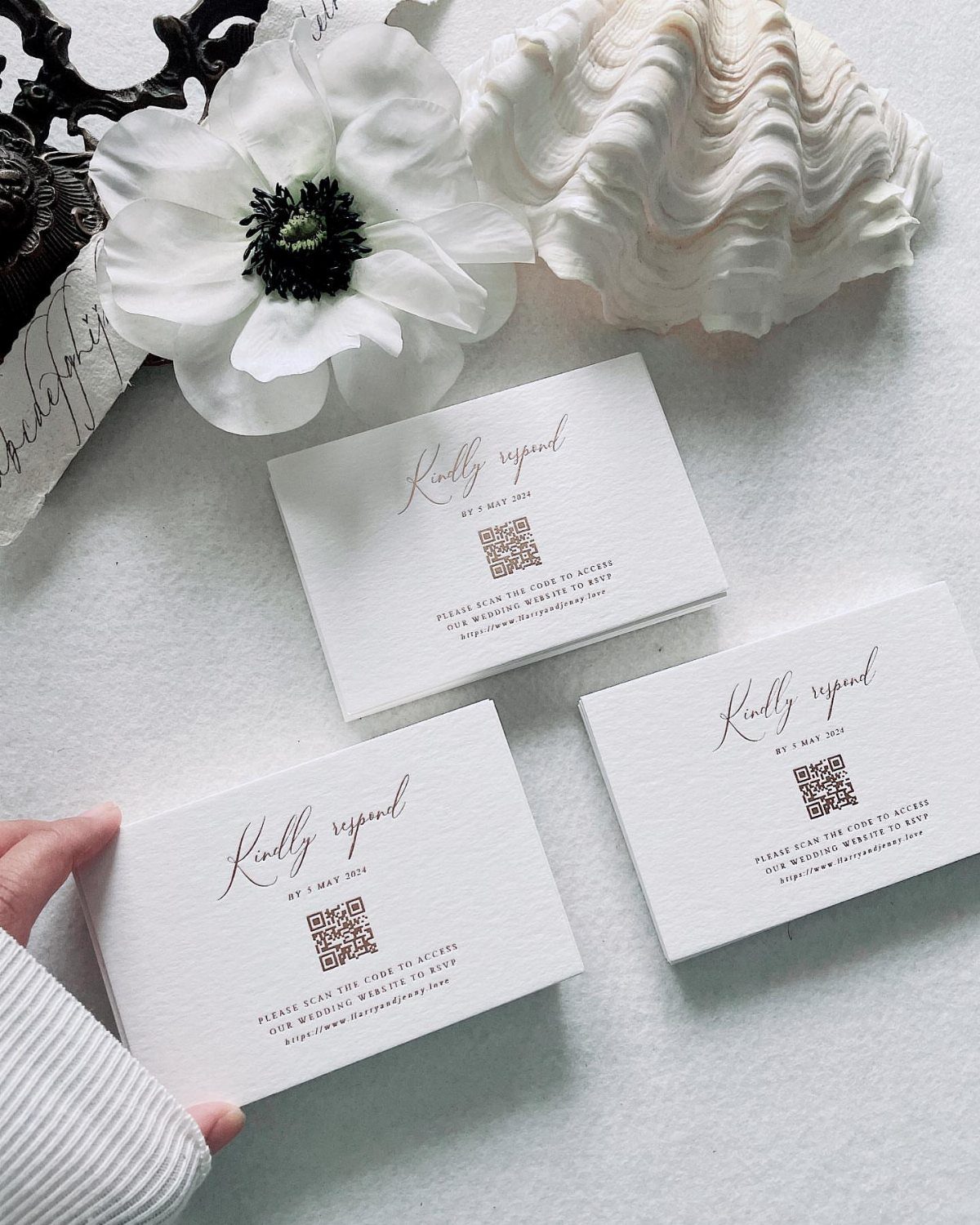 Three white RSVP cards with QR codes, a white flower, and a seashell.
