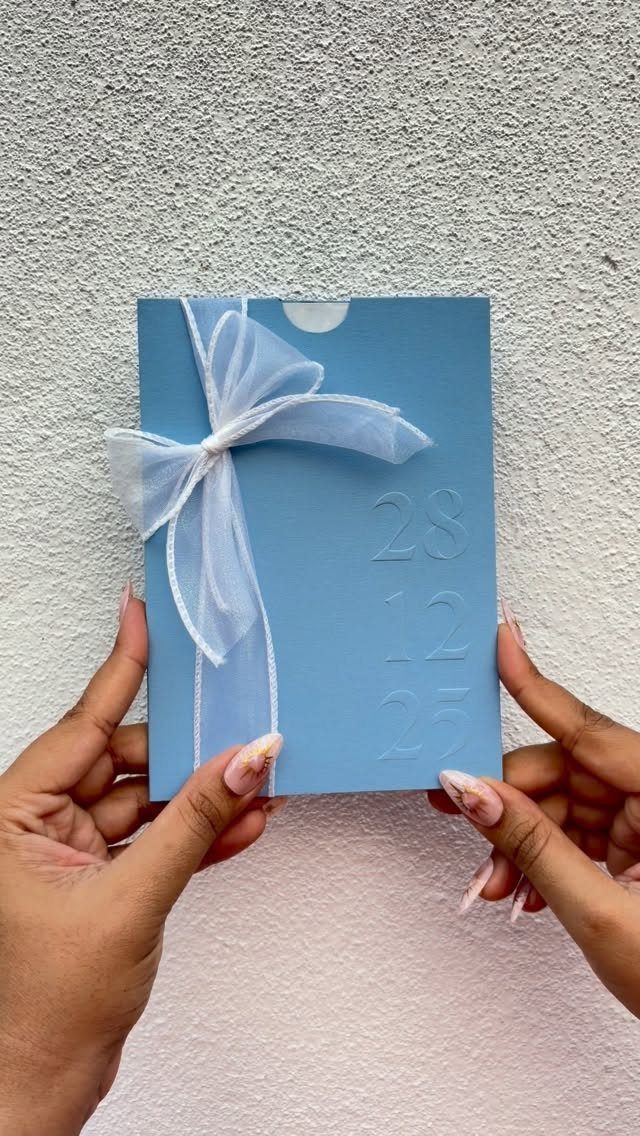 Light blue invitation envelope tied with a white sheer ribbon bow and embossed numbers.