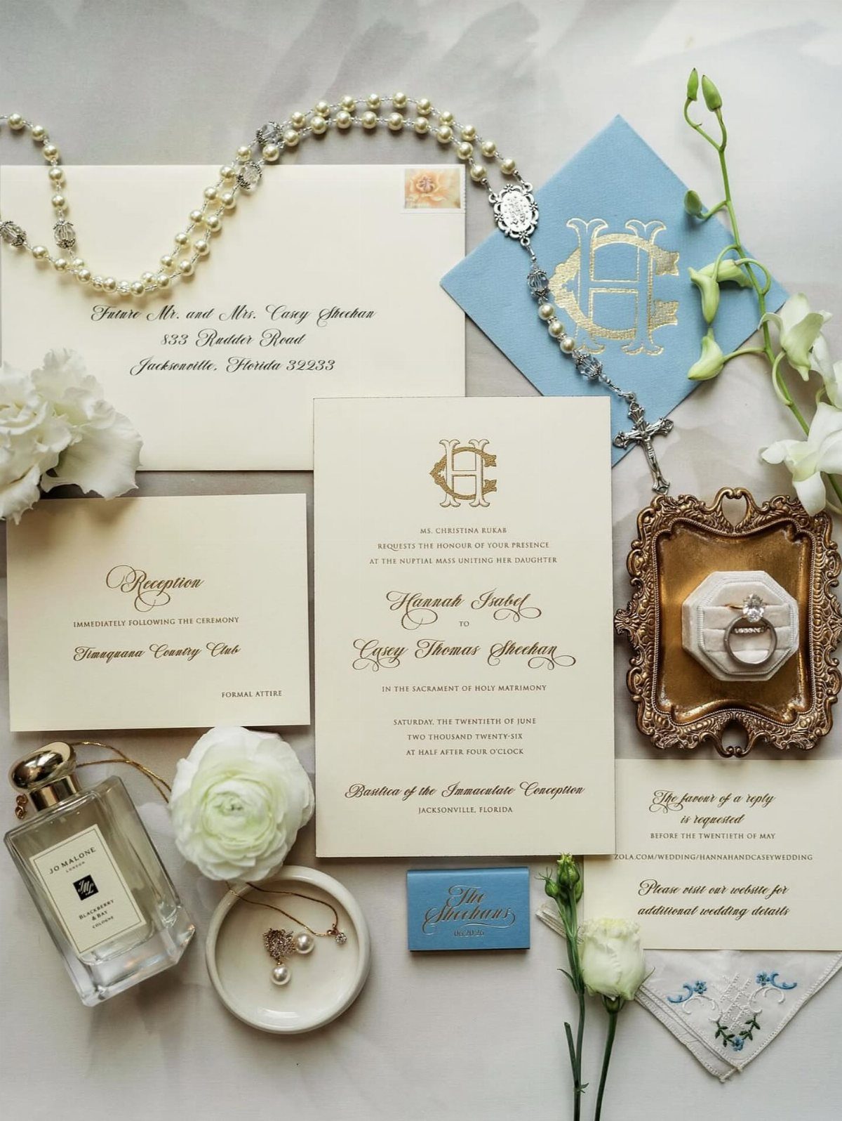 Wedding invitation suite with cream cards, blue envelope, pearls, and white floral accents.