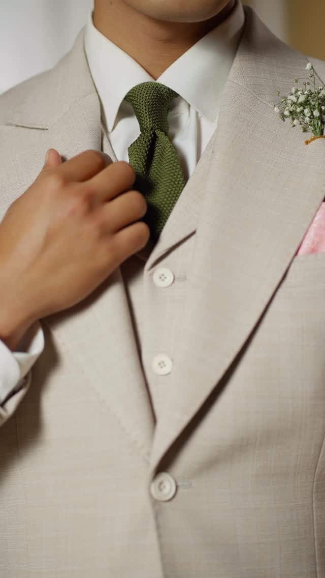 Beige three-piece wedding suit with a green tie and white floral boutonniere.