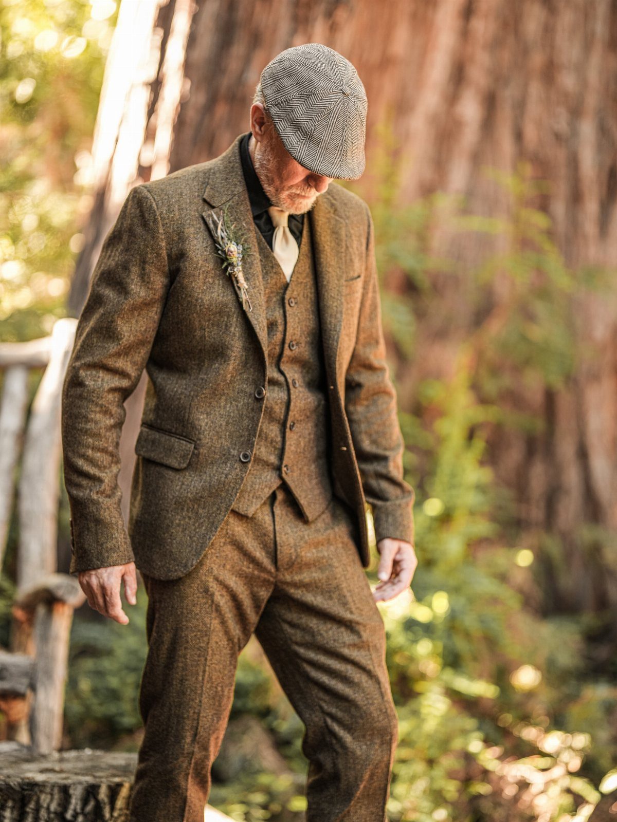 Man in brown tweed three-piece suit and flat cap standing in a forest
