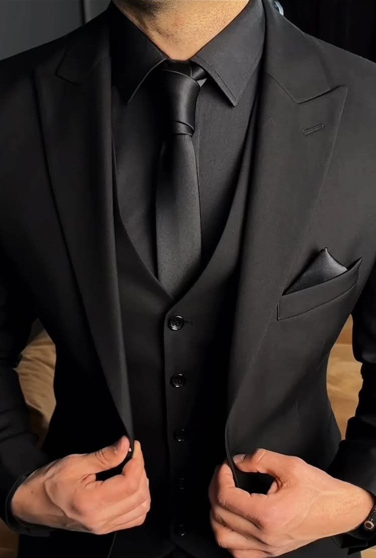 Man in a formal all-black three-piece suit with a matching tie and pocket square.