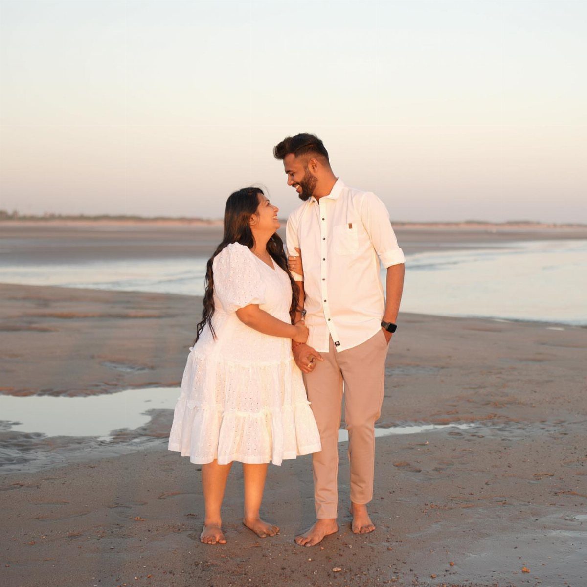 Man in white shirt and beige trousers with woman in white dress on beach