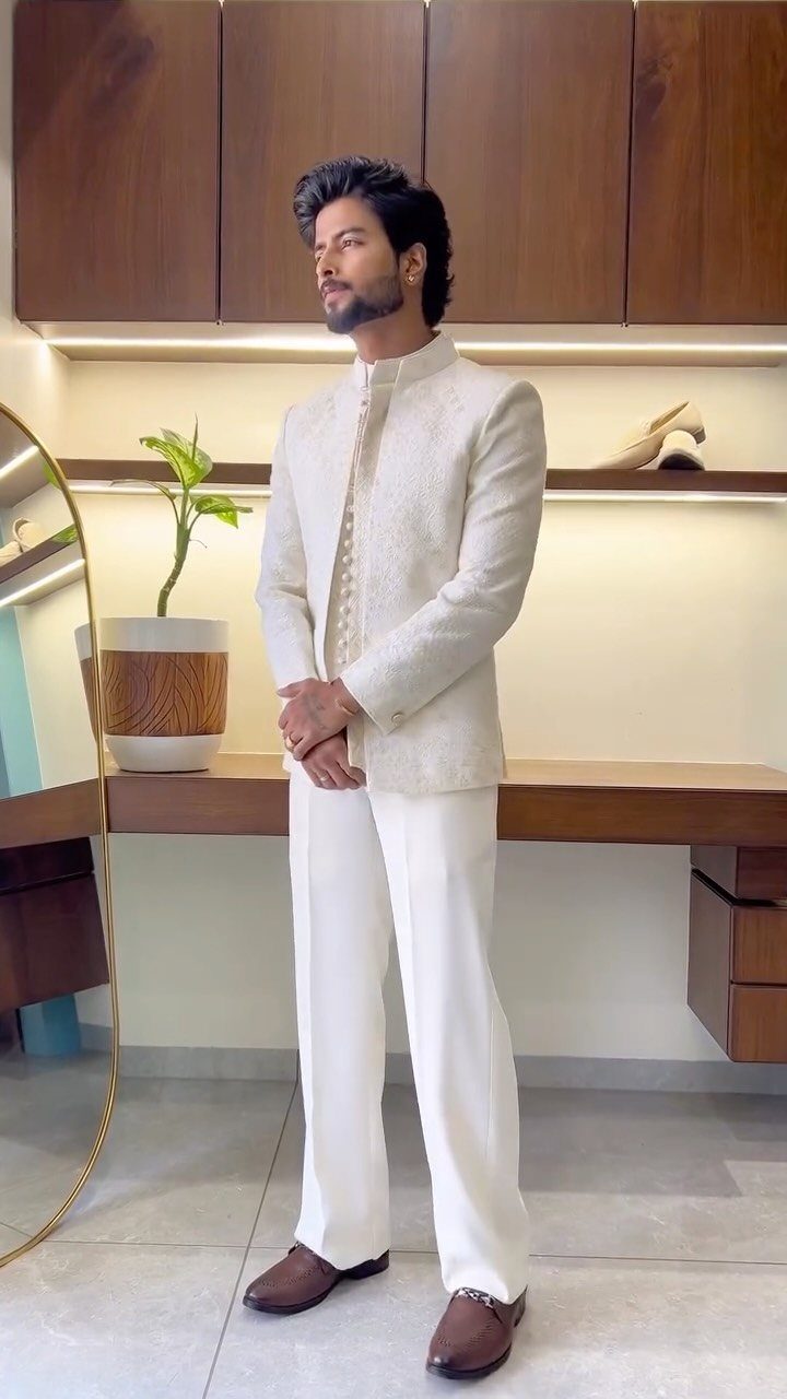 Man wearing a white embroidered bandhgala jacket and white trousers with brown loafers.