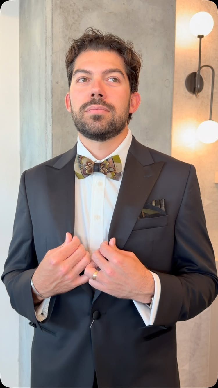 Man in a navy suit wearing a patterned bow tie and dark pocket square.