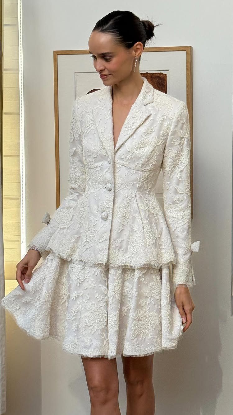 Woman in a white lace bridal blazer and matching short flared skirt.