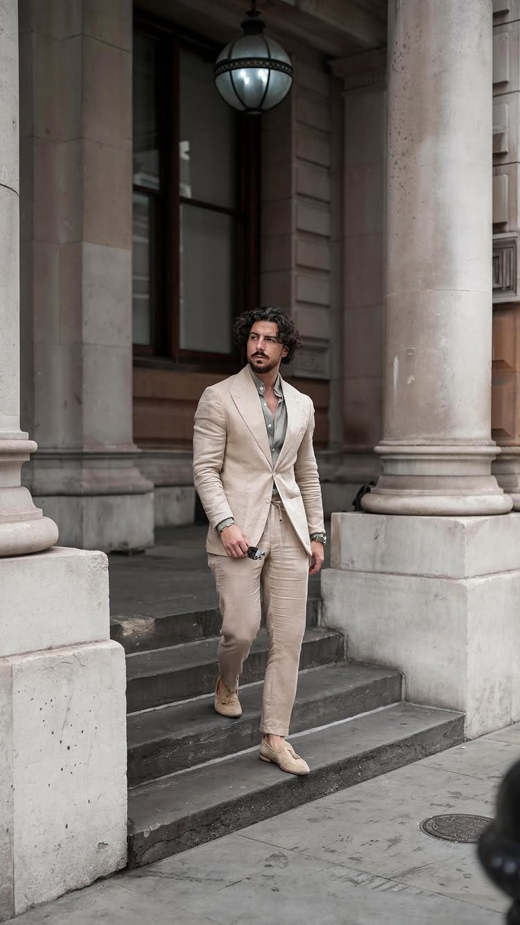 Man in a light beige linen suit standing on stone steps by columns.