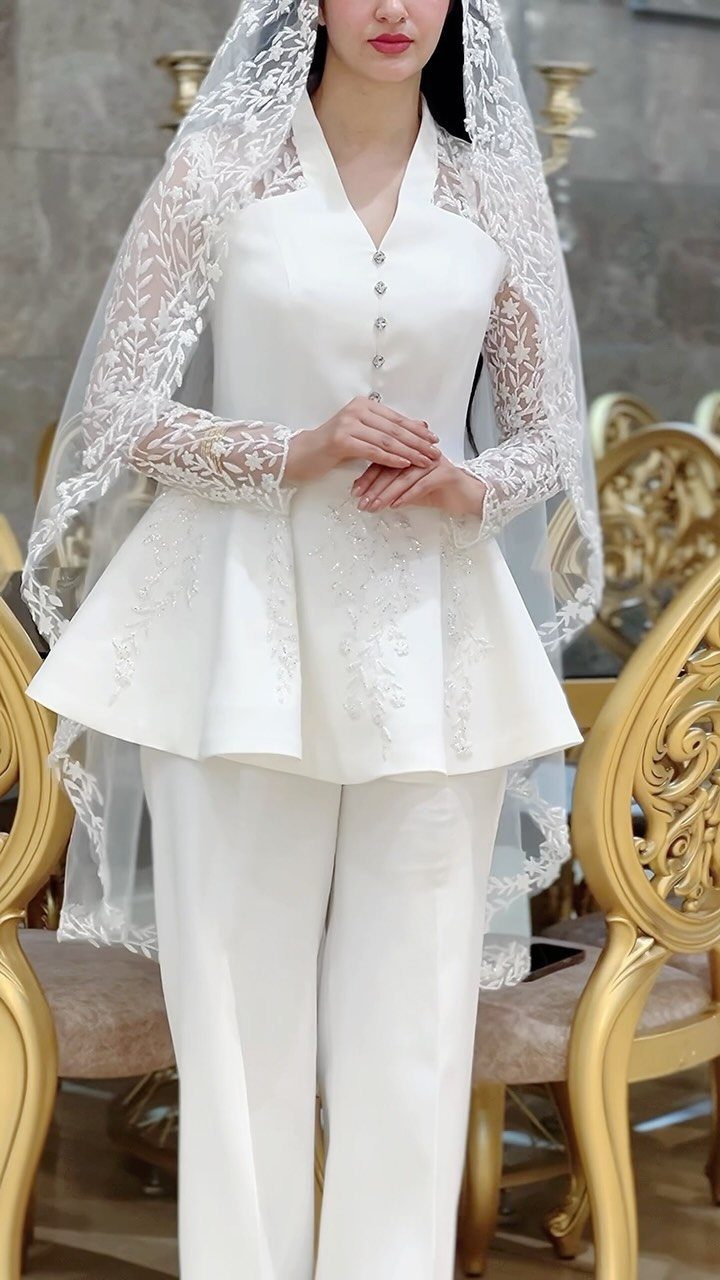 Bride wearing a white peplum wedding suit and a long lace veil.
