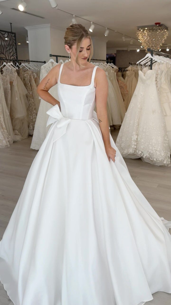 Woman in a white A-line wedding dress with a bow in a bridal shop.