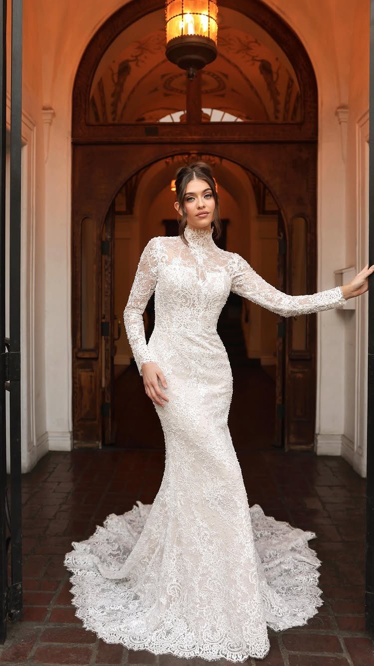 Woman in a high-neck white lace wedding dress posing in an arched doorway.